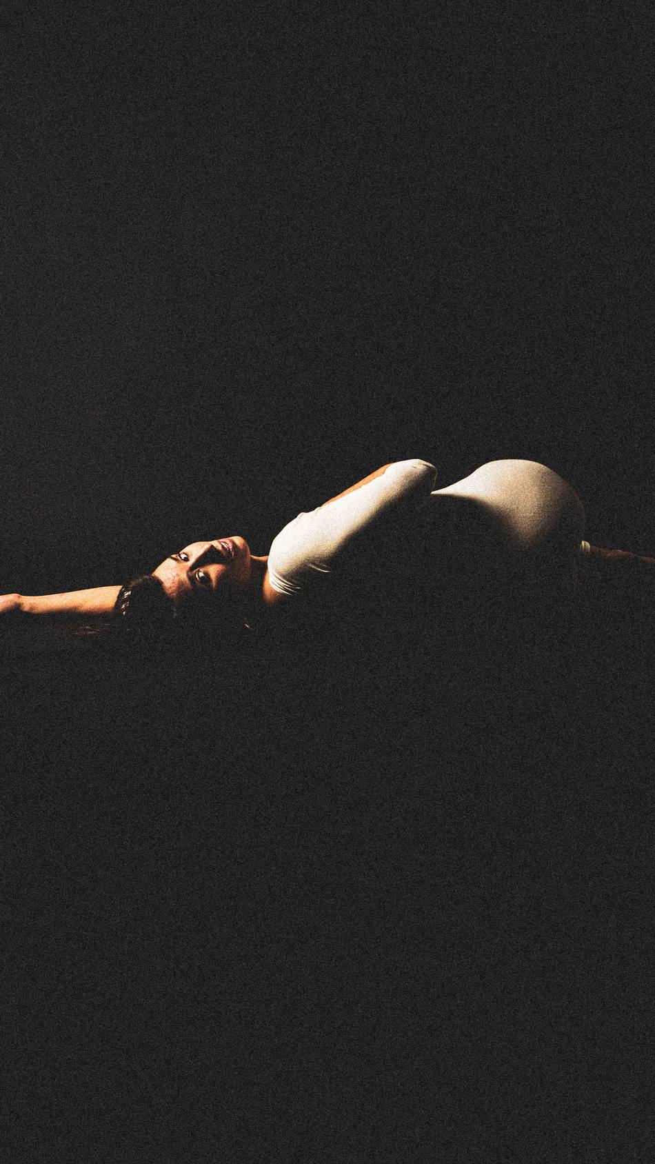 Dancer curled low under a single warm light