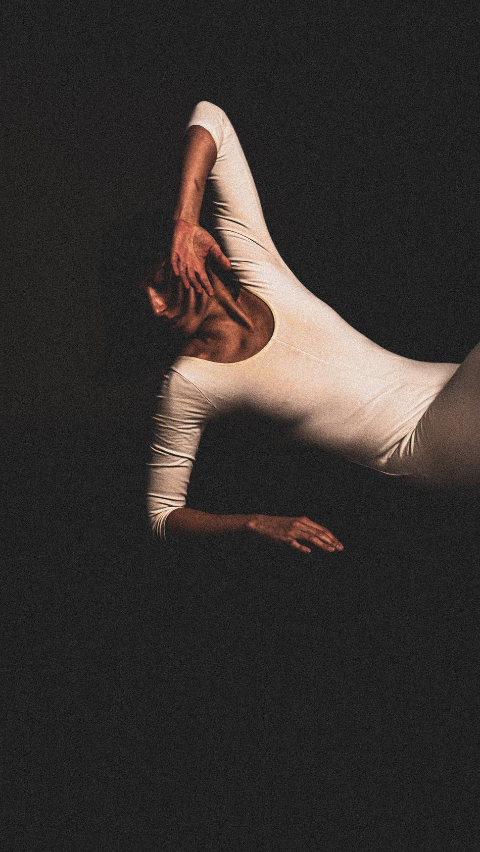 Dancer shielding her face, one leg extended in silhouette