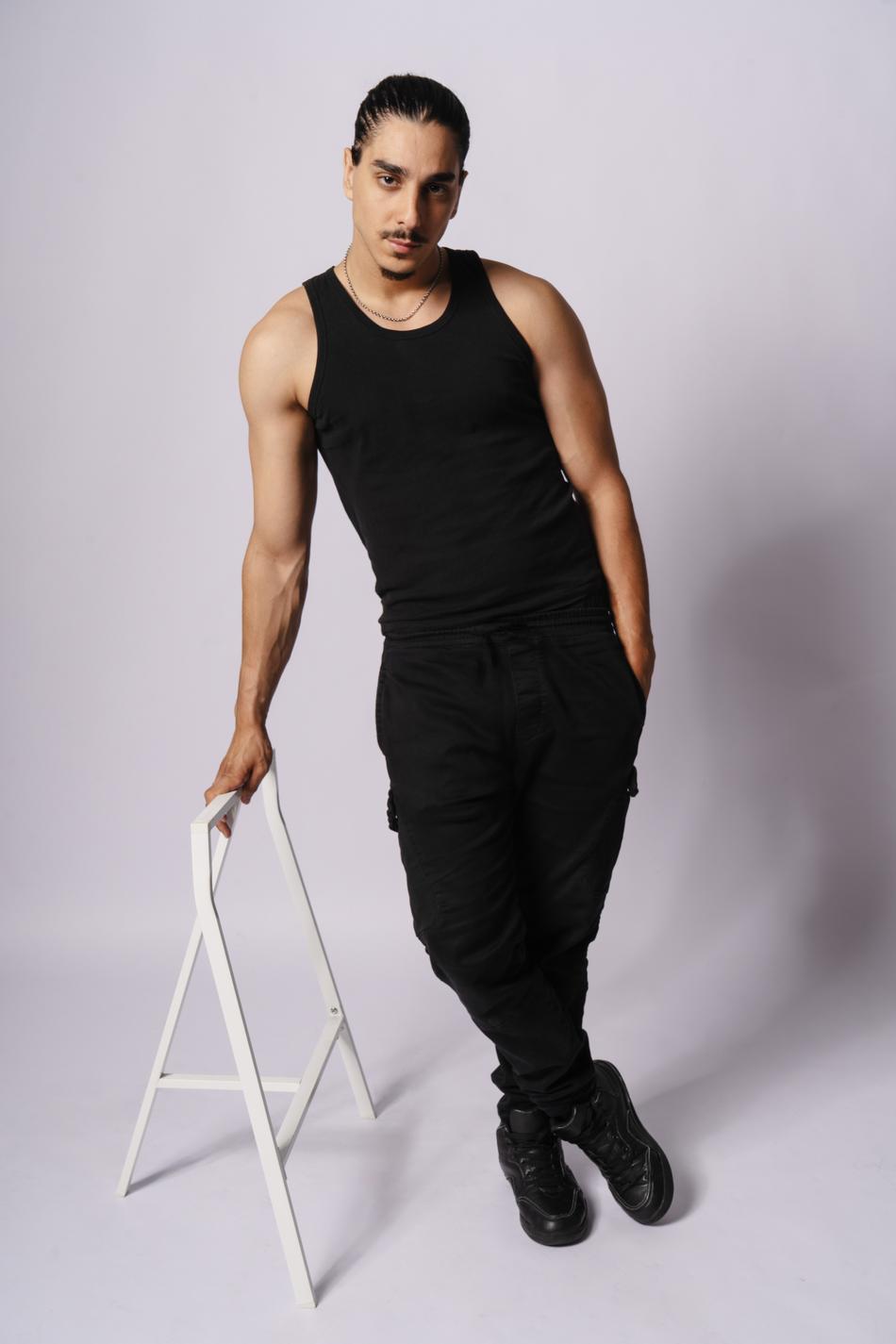 Actor standing full-length, hand on a white sawhorse stool