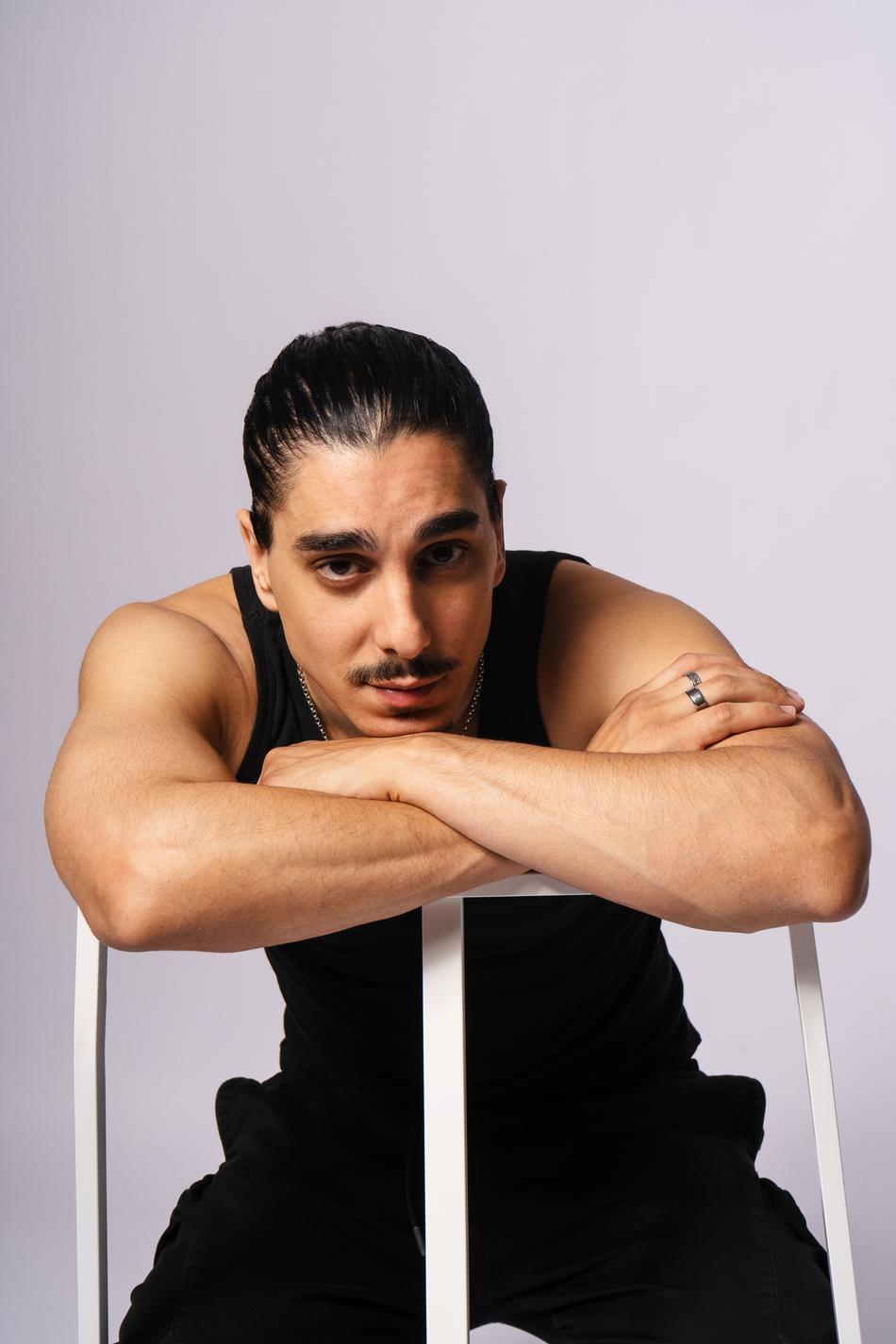 Actor leaning forward on a stool, arms crossed under chin