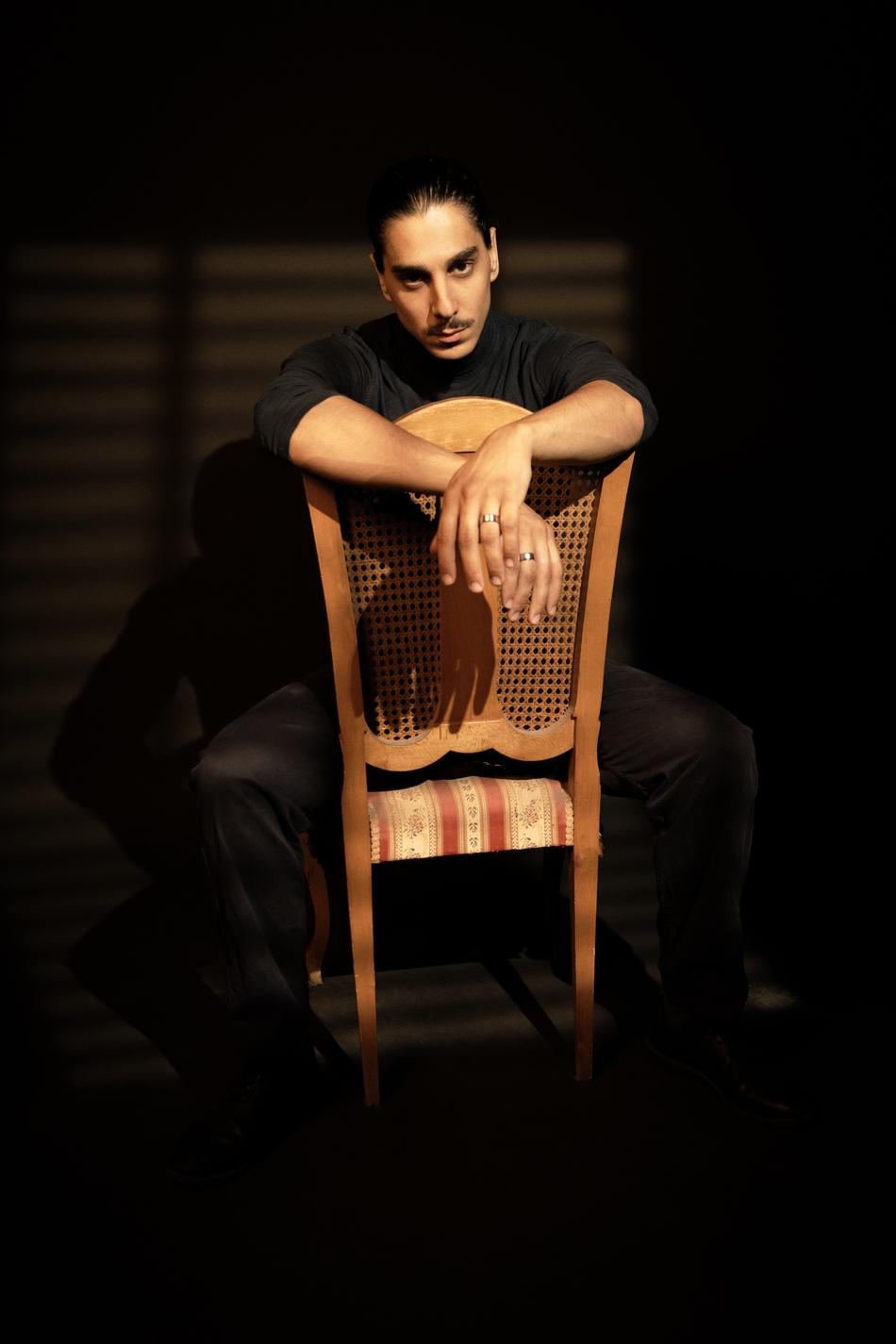 Actor seated backwards on a cane chair, hands clasped