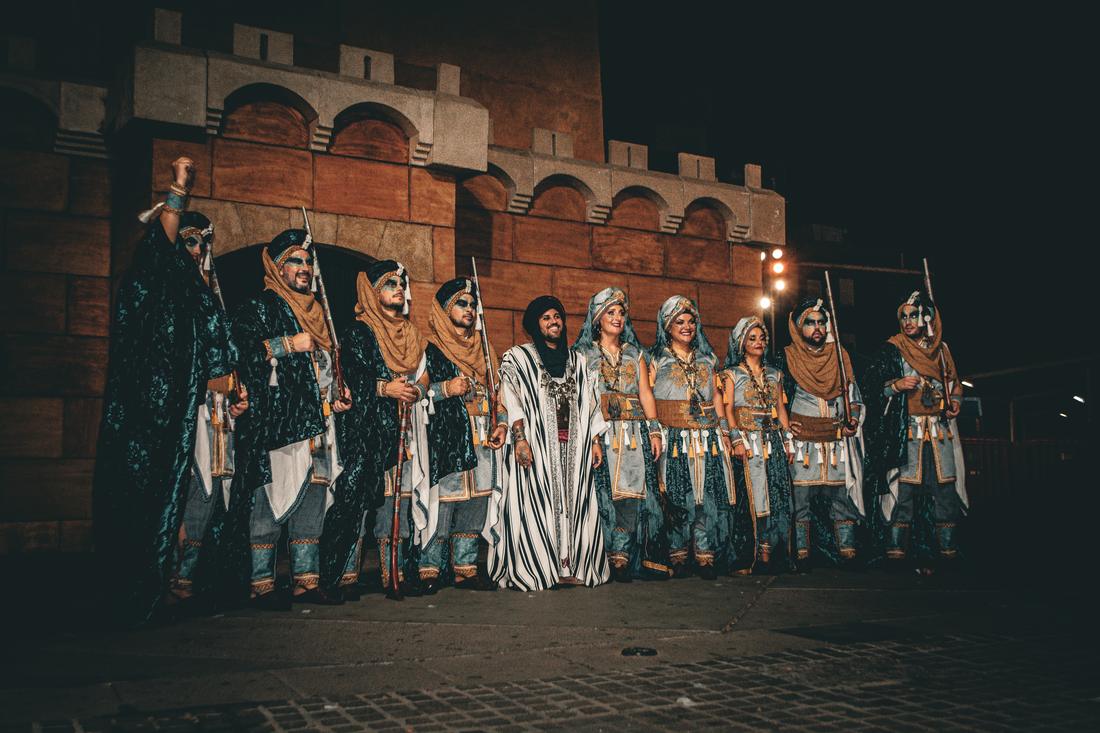 Group of Moros in teal costume assembled before a stone wall