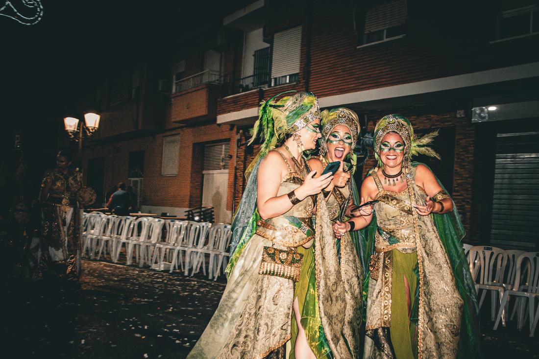 Three women in green and gold costume laughing at a phone
