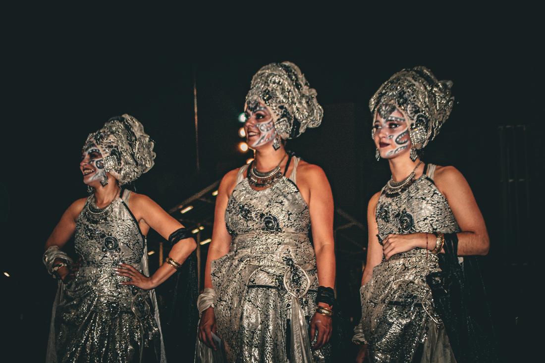 Three women in silver costume laughing together at night