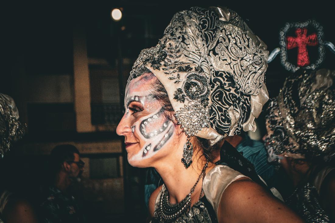 Profile portrait of a woman in ornate face paint with a red cross emblem behind her