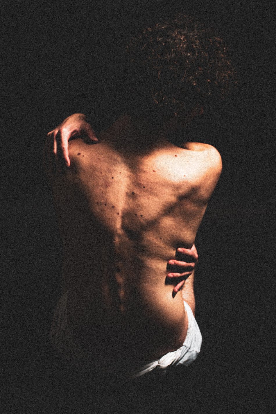 Man seen from behind, back arched, one hand reaching to his shoulder