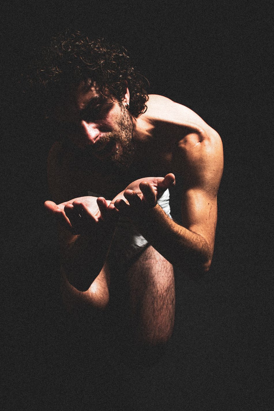 Man crouched low, hands cupped and reaching forward, gaze cast down